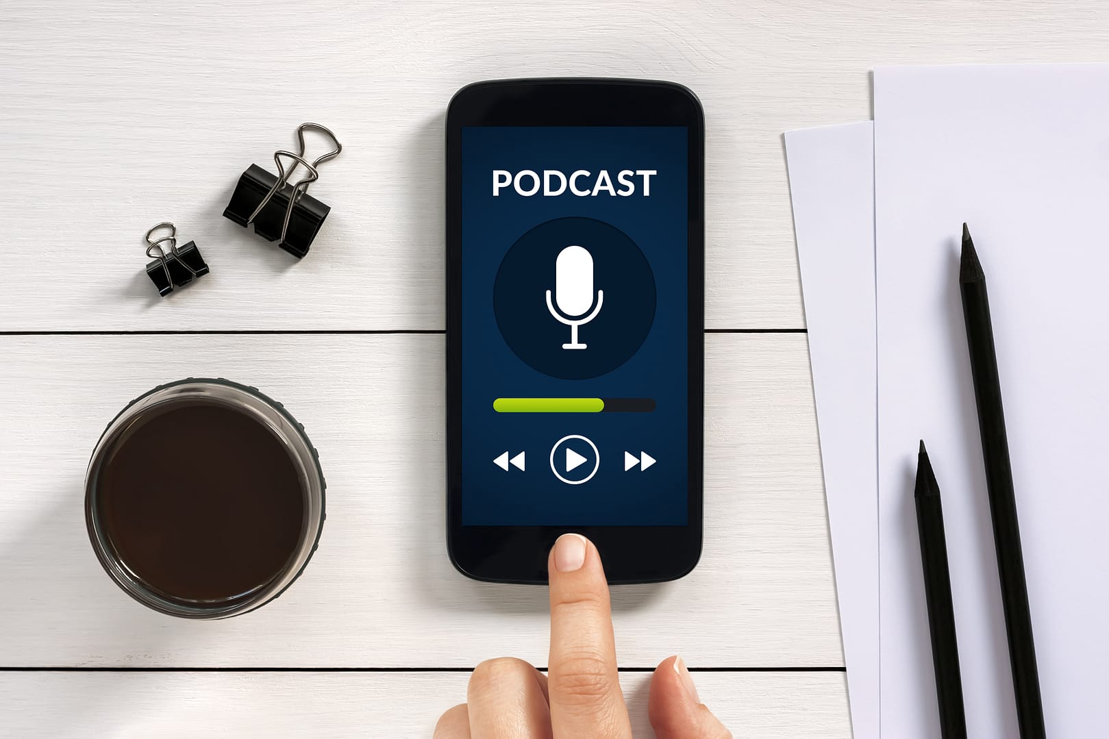 Podcast concept on smart phone screen with office objects on white wooden table. All screen content is designed by me. Flat lay